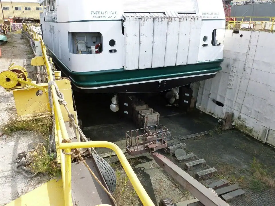 A white-and-green ferry sits in a concrete dry dock beside yellow industrial railings and machinery.