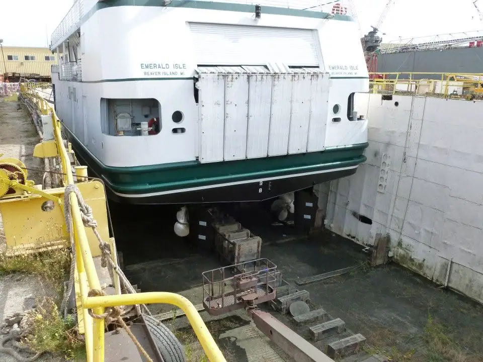 A white-and-green ferry sits elevated in a concrete dry dock surrounded by yellow equipment and rails.