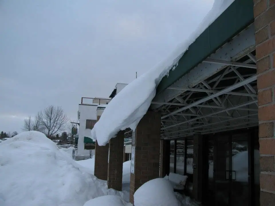 A glass-doored entrance is nearly buried beneath deep snow along a brick-supported canopy.