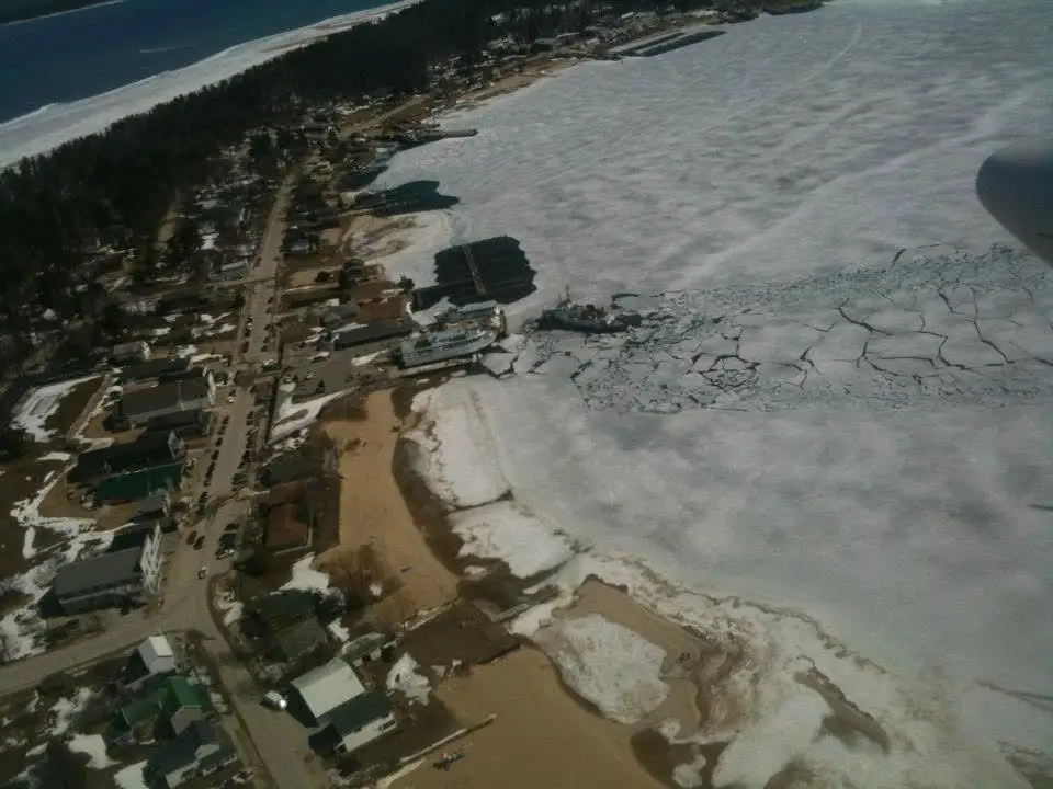 Aerial view of a shoreline settlement, ferry, and broken ice in a frozen harbor.