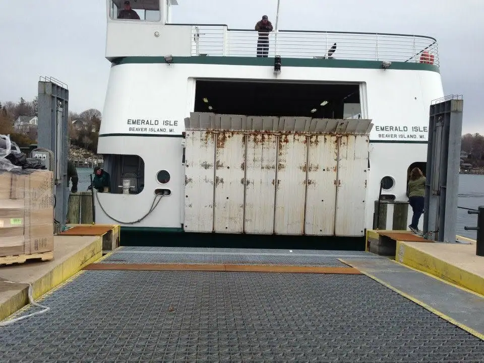 Ferry with an open vehicle bay and rusted loading door at a pier.