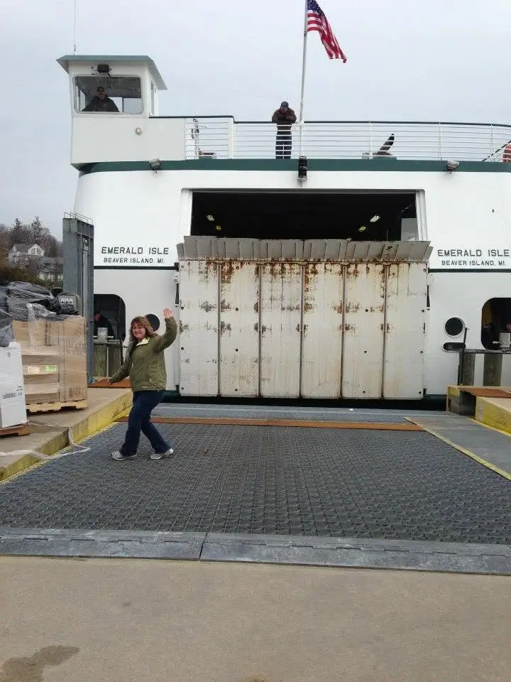A woman waves on a vehicle loading deck in front of a large white ferry.