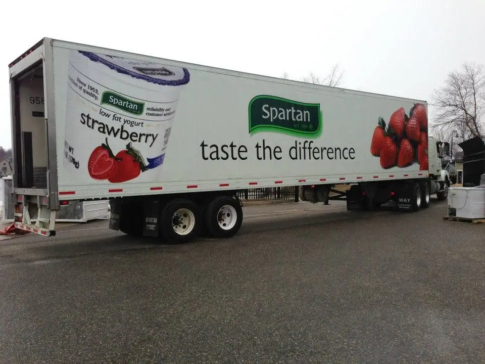 A white semi-trailer displays a Spartan strawberry yogurt advertisement with a large yogurt cup and fresh strawberries.