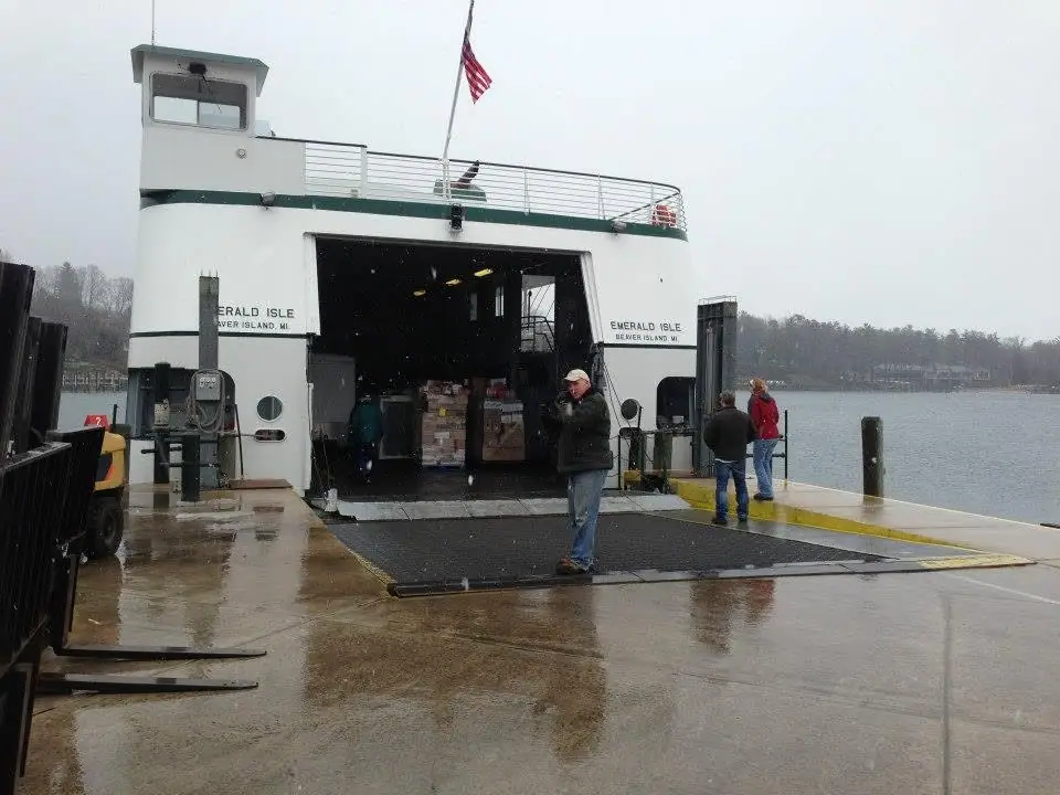 A ferry with its stern cargo door open at a wet pier during precipitation.
