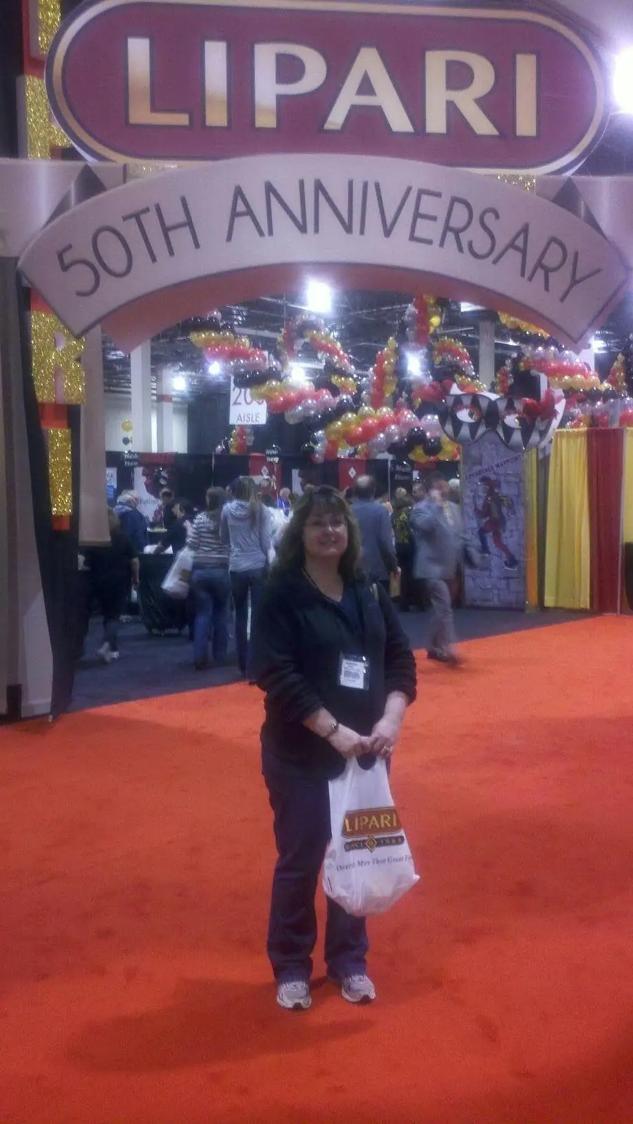 A woman stands on a red-carpeted trade-show aisle in front of a decorated food-distribution booth.