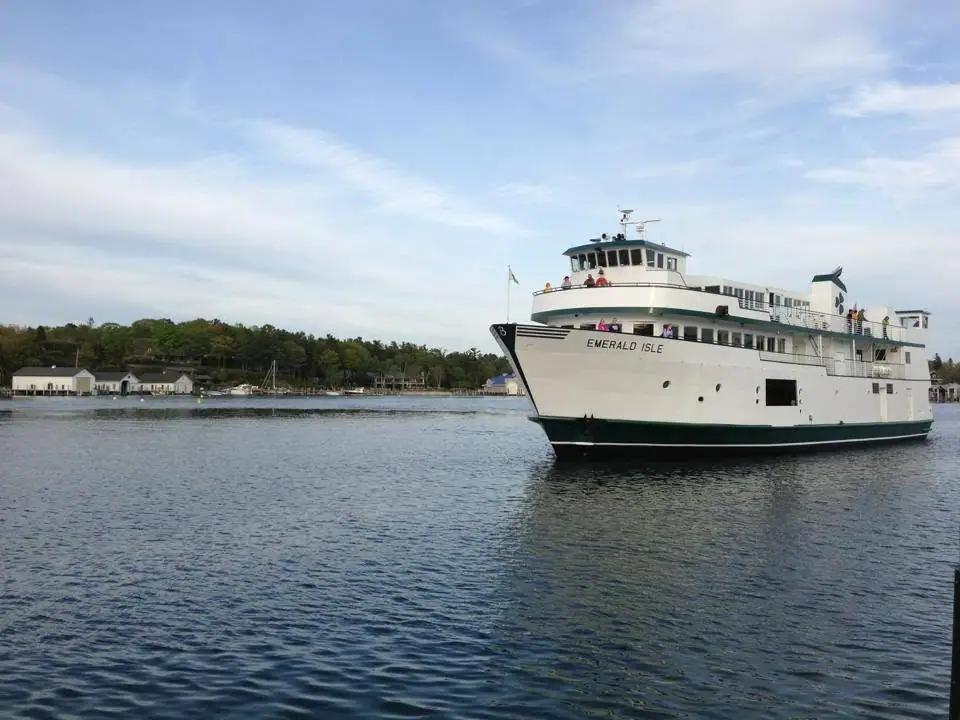 A white passenger ferry marked “EMERALD ISLE” moves across calm water near a wooded shoreline.