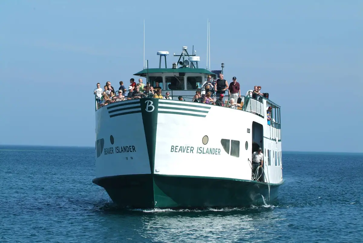 White-and-dark-green ferry carrying many passengers approaches across open water.