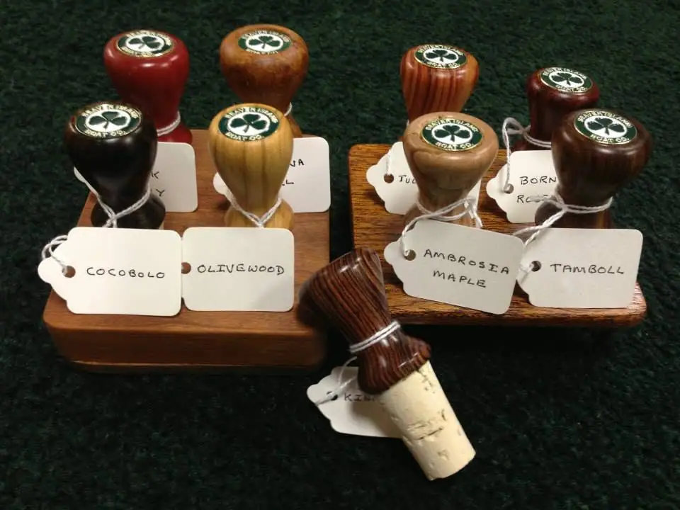 Assorted turned wooden wine stoppers with handwritten wood-name tags arranged on display trays.