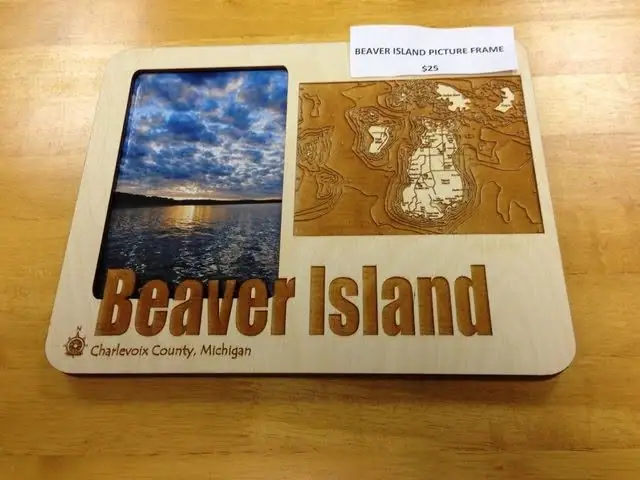 A wooden picture frame displays a sunset photograph, a raised relief map, large lettering, and a $25 price label.