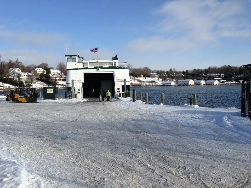 White ferry with an open loading door at a snow-covered dock, with a forklift and two people nearby.