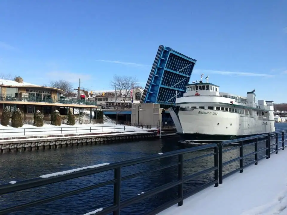 A white ferry sits beside a raised blue drawbridge in a snowy waterfront scene.
