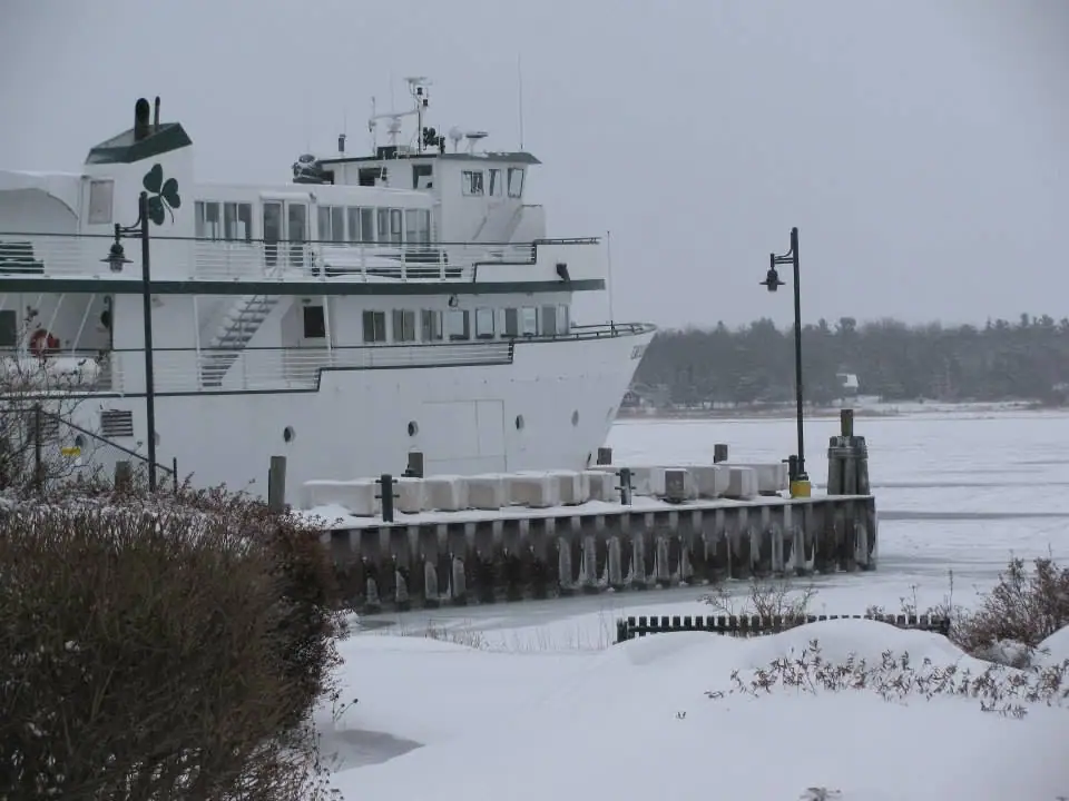 A white passenger ferry is docked beside a snow-covered pier in winter.