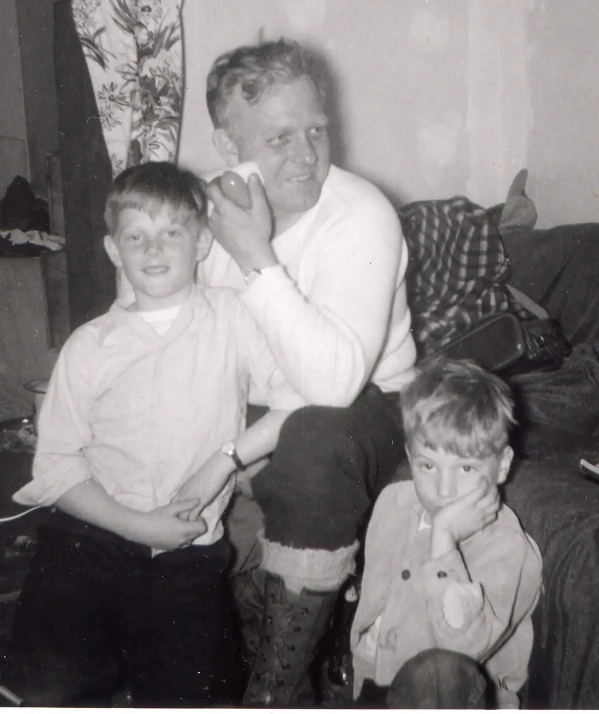 Black-and-white photograph of an adult man with two boys seated on a couch indoors.