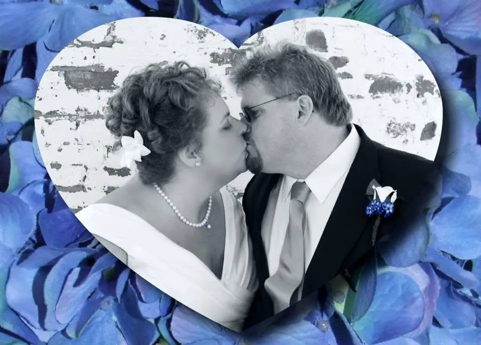 A couple in wedding attire kisses inside a heart-shaped frame surrounded by blue flowers.