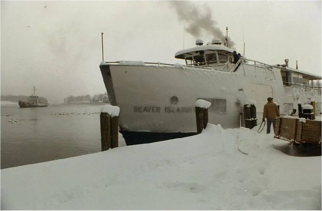 A snow-covered ferry is moored at a pier while smoke rises from its upper deck.
