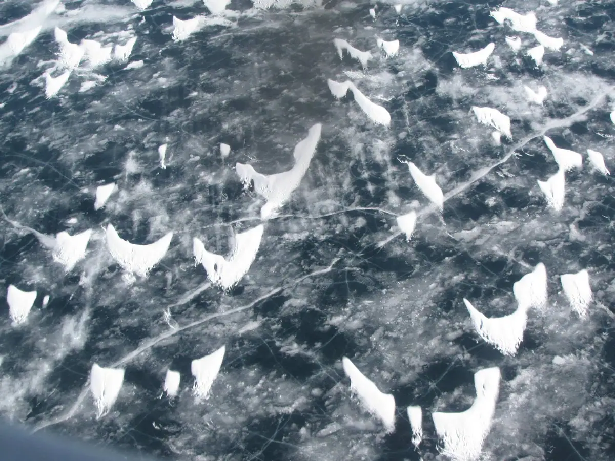 Aerial view of dark ice covered with scattered white snow formations and cracks.