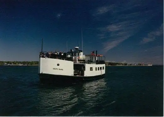 White passenger ferry traveling across dark water with people gathered on its upper deck.