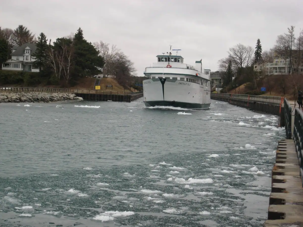 A white ferry approaches through ice-strewn water between waterfront walkways.