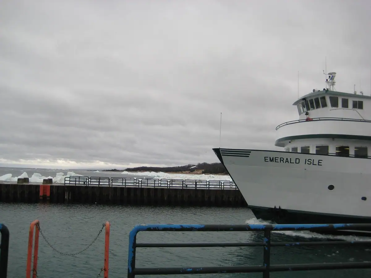 A white ferry marked “EMERALD ISLE” passes a pier with ice along the distant shoreline.