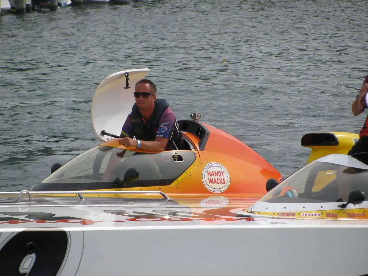 A man sits in an orange powerboat beside another brightly colored boat on rippling water.