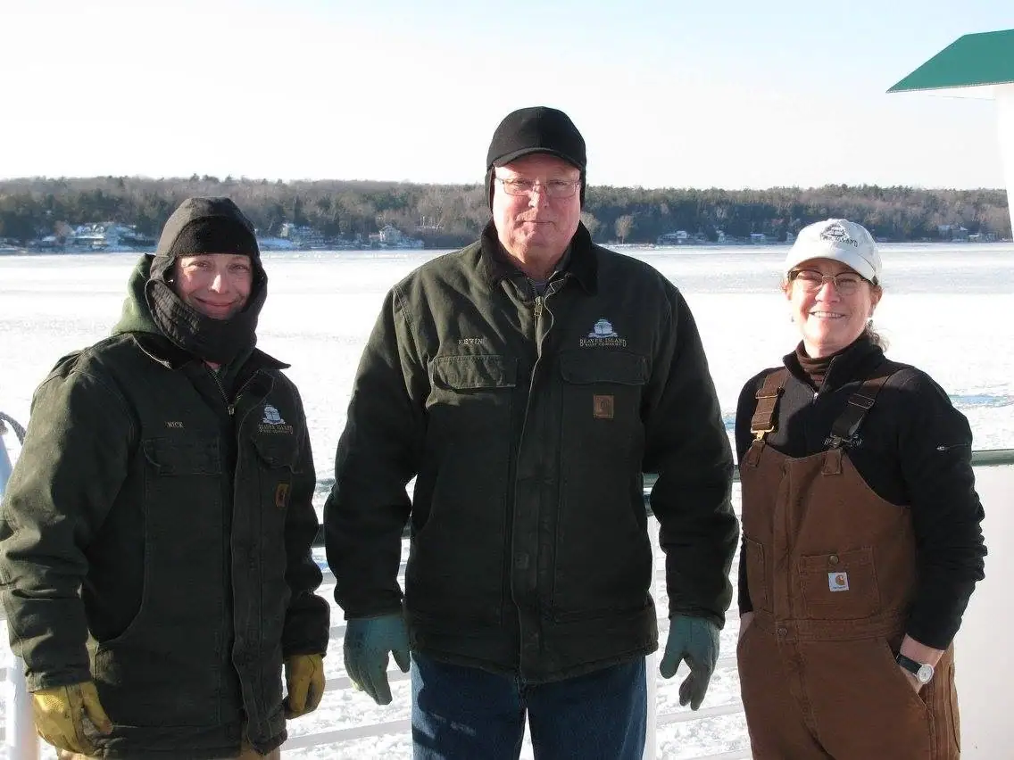 Three workers pose on a boat deck in winter clothing beside ice-covered water.