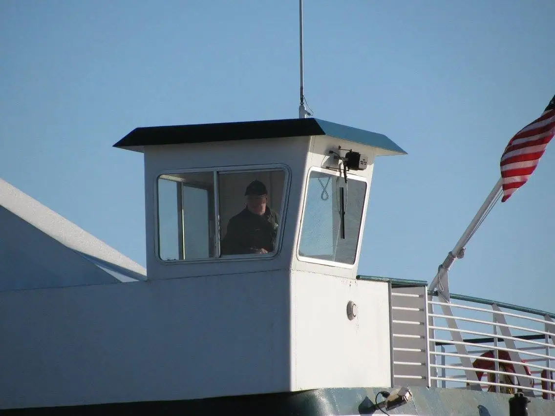 Close view of a white vessel wheelhouse with a person inside and an American flag flying beside it.