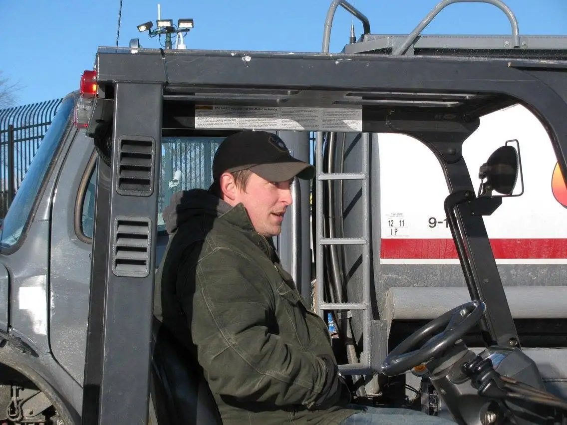 A person sits in the cab of a gray emergency truck with a ladder and red stripe.