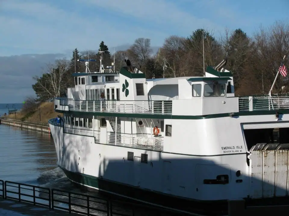 A white multi-deck ferry with green trim is alongside a dock, with an American flag at the stern.