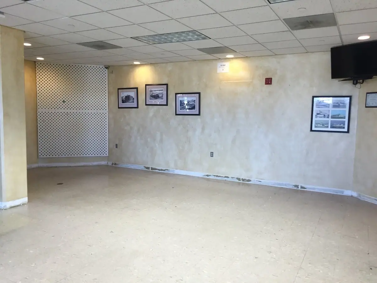 Empty commercial room with a lattice partition, framed photographs, a wall-mounted television, and a small sale sign.