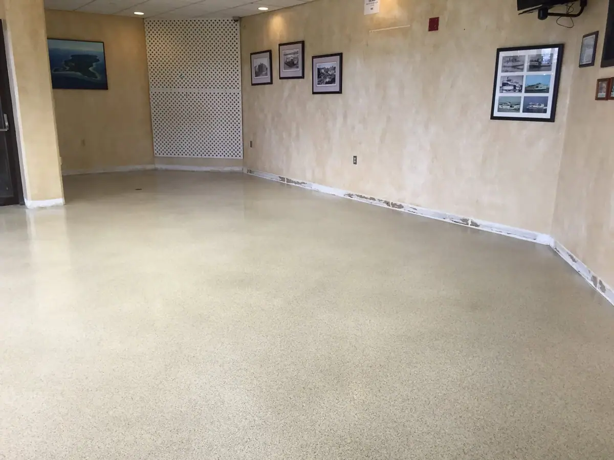 Empty interior room with yellow walls, a speckled floor, framed images, and a white lattice screen.