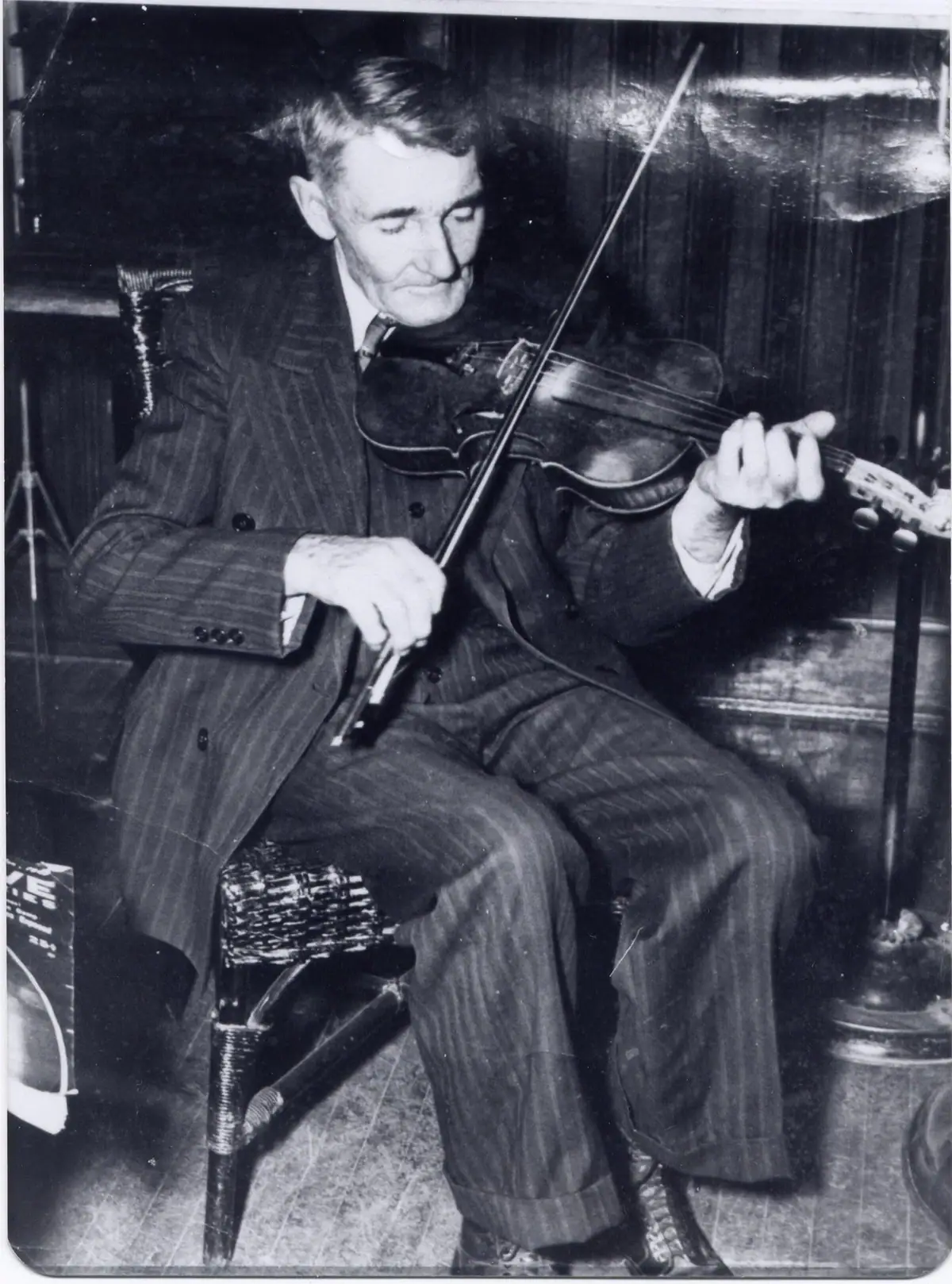 Black-and-white portrait of a seated man playing a violin in a pinstriped suit.