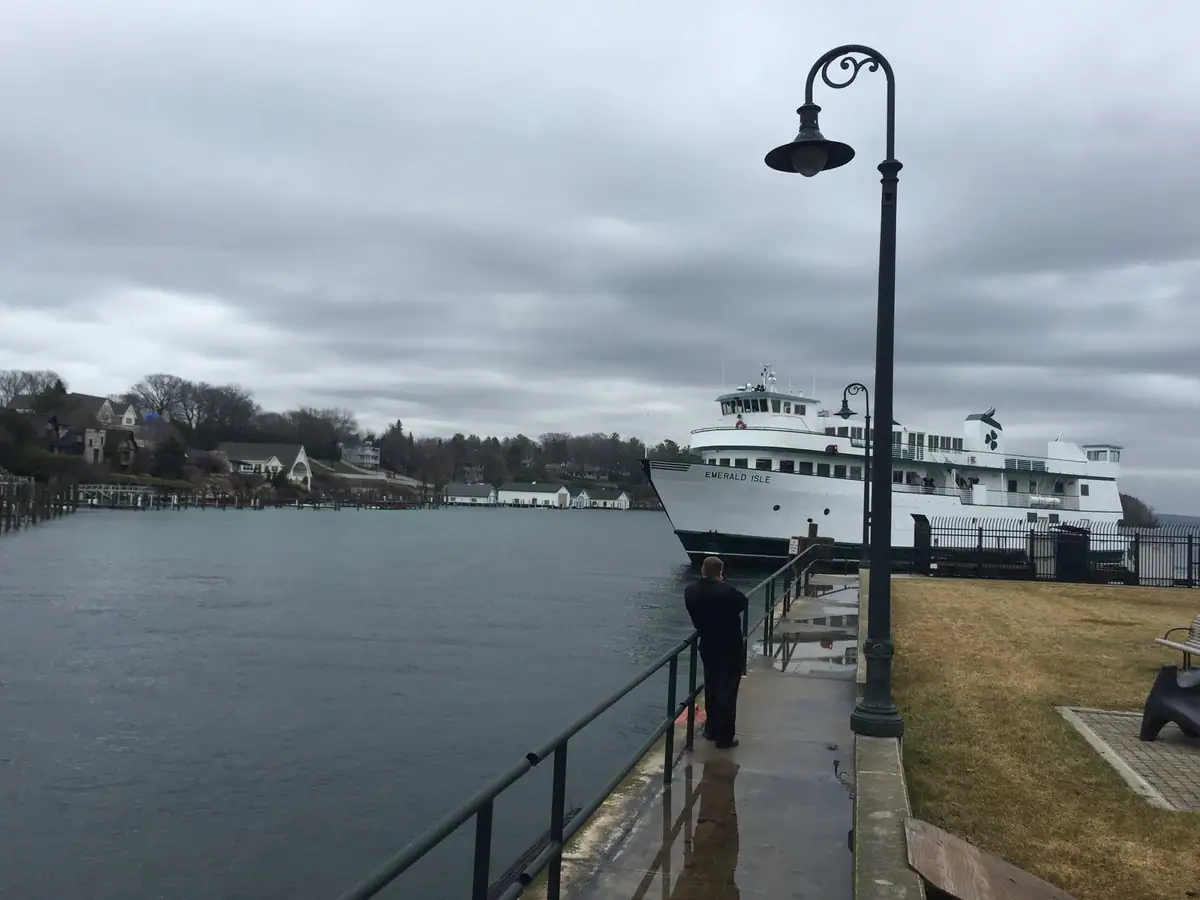 A white ferry named EMERALD ISLE is docked beside a wet waterfront walkway beneath heavy clouds.