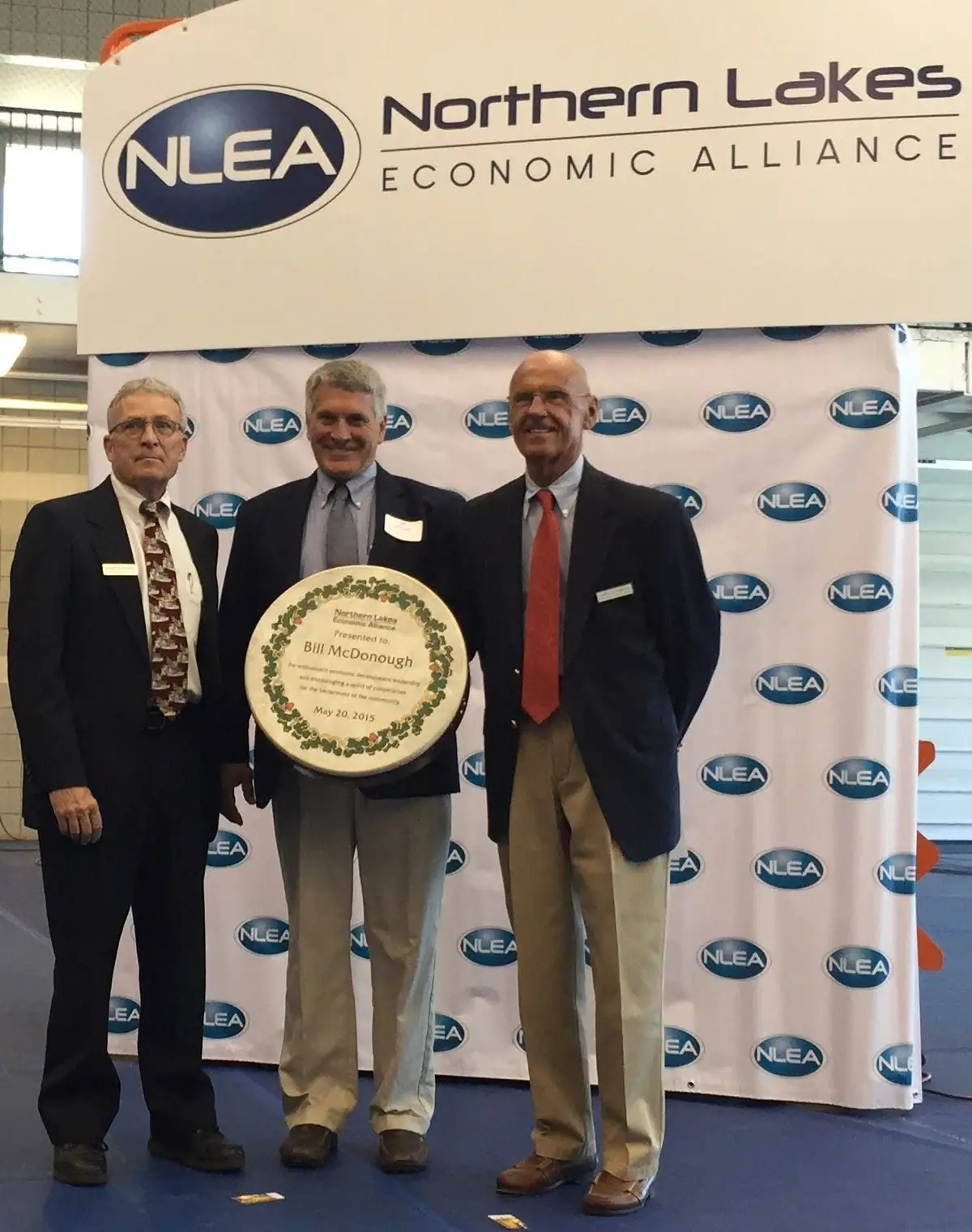 Three men pose with a decorated award cake beneath an NLEA sign and branded backdrop.