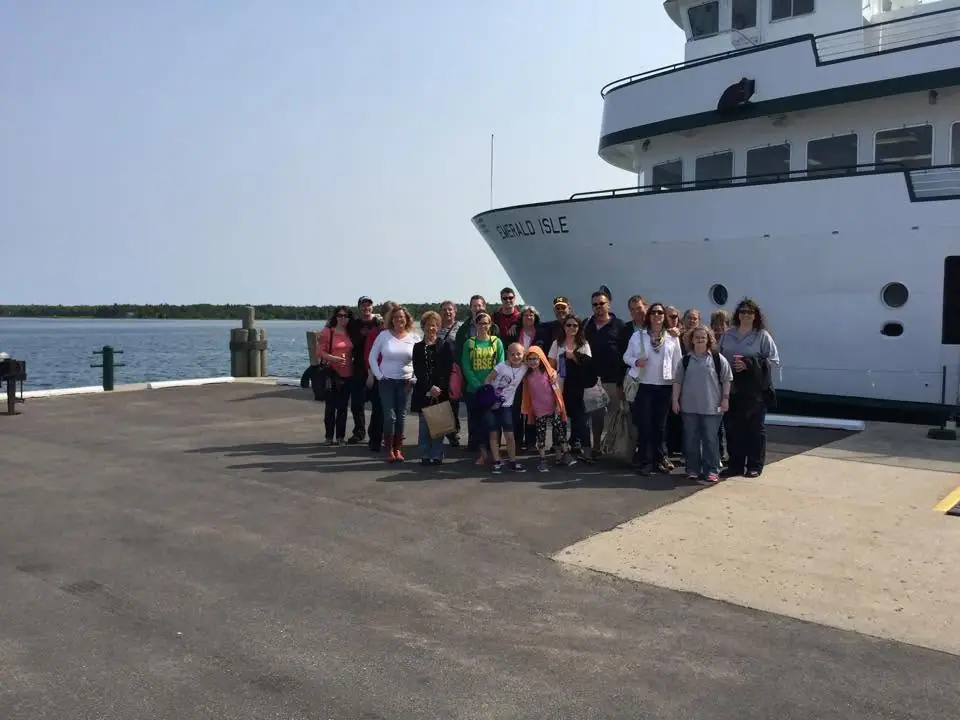 A group poses on a dock beside the large white ferry EMERALD ISLE.