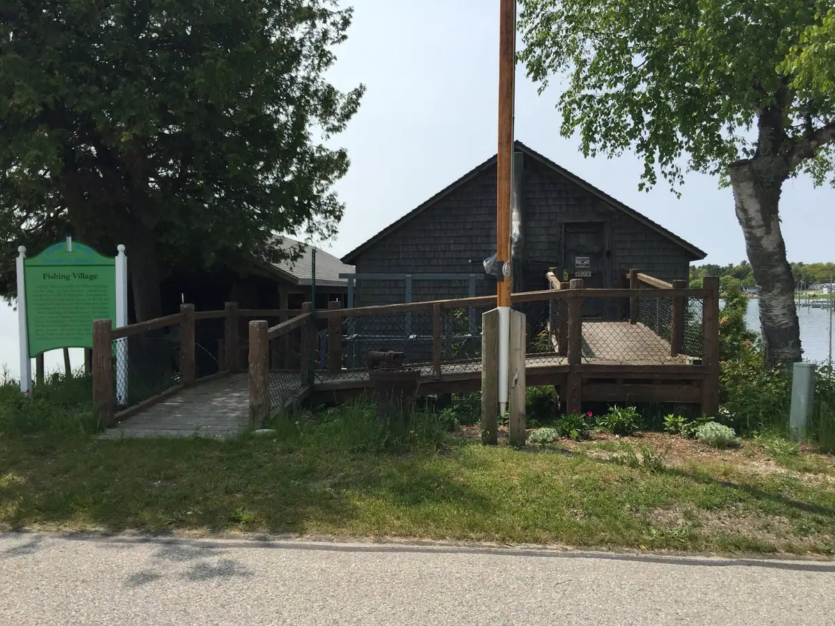 A shingled waterfront building with a wooden deck and a green “Fishing Village” sign.
