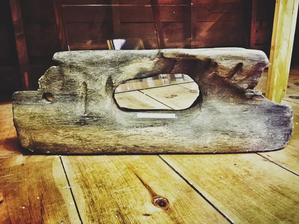 A weathered wooden block with a large oval opening rests on a wooden floor indoors.