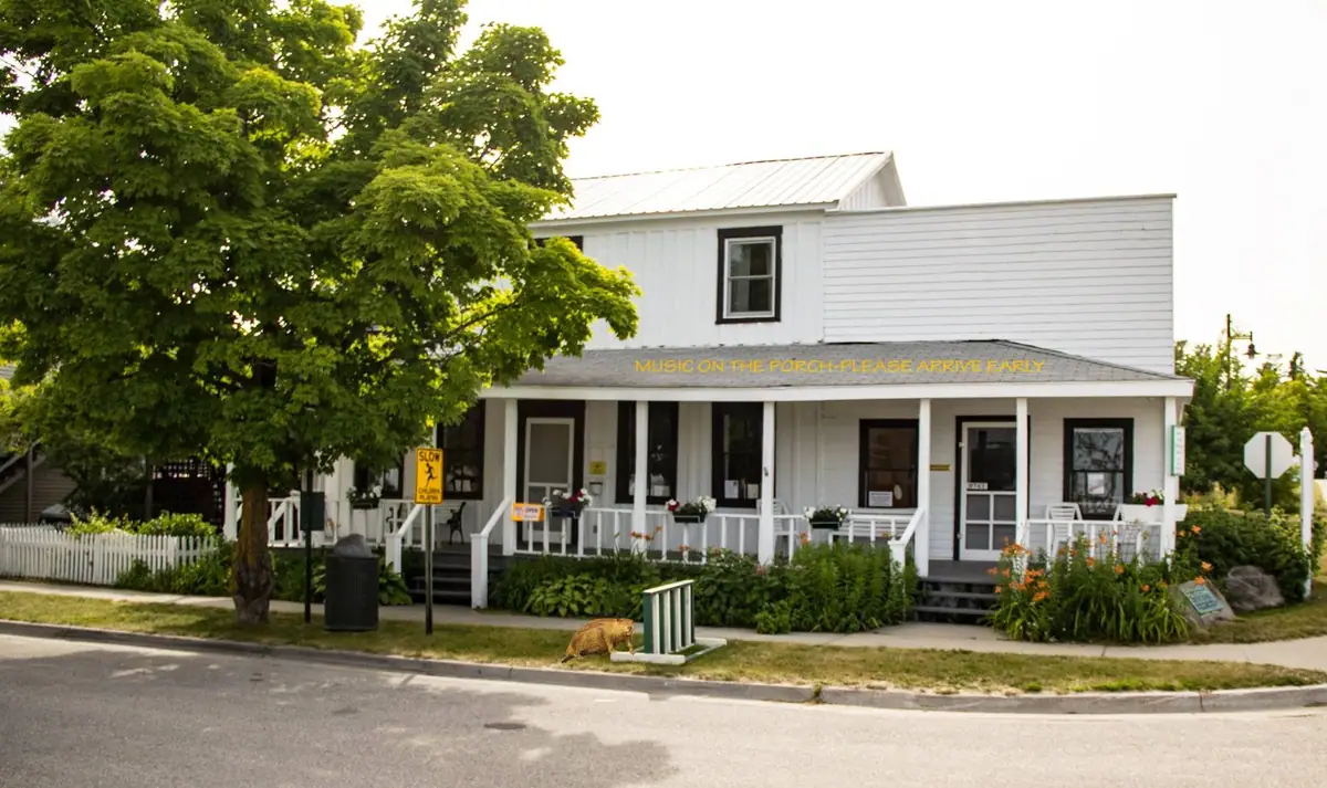 White two-story building with a porch, street frontage, and a small brown animal near the curb.