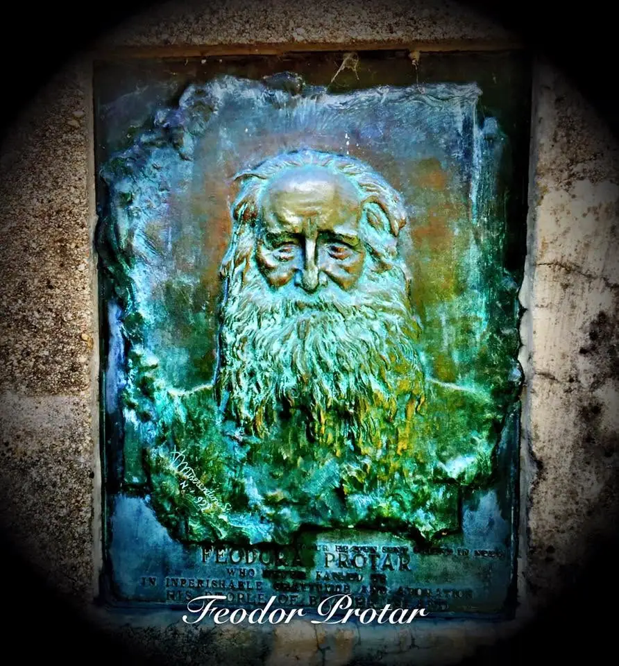 Weathered blue-green relief portrait of an elderly bearded man mounted on an inscribed plaque.