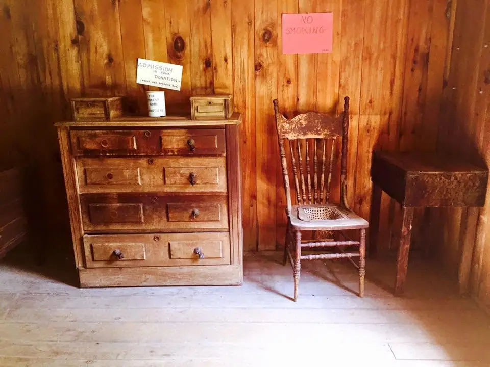Wooden bedroom furniture and chairs displayed in a wood-paneled room with admission and no-smoking signs.