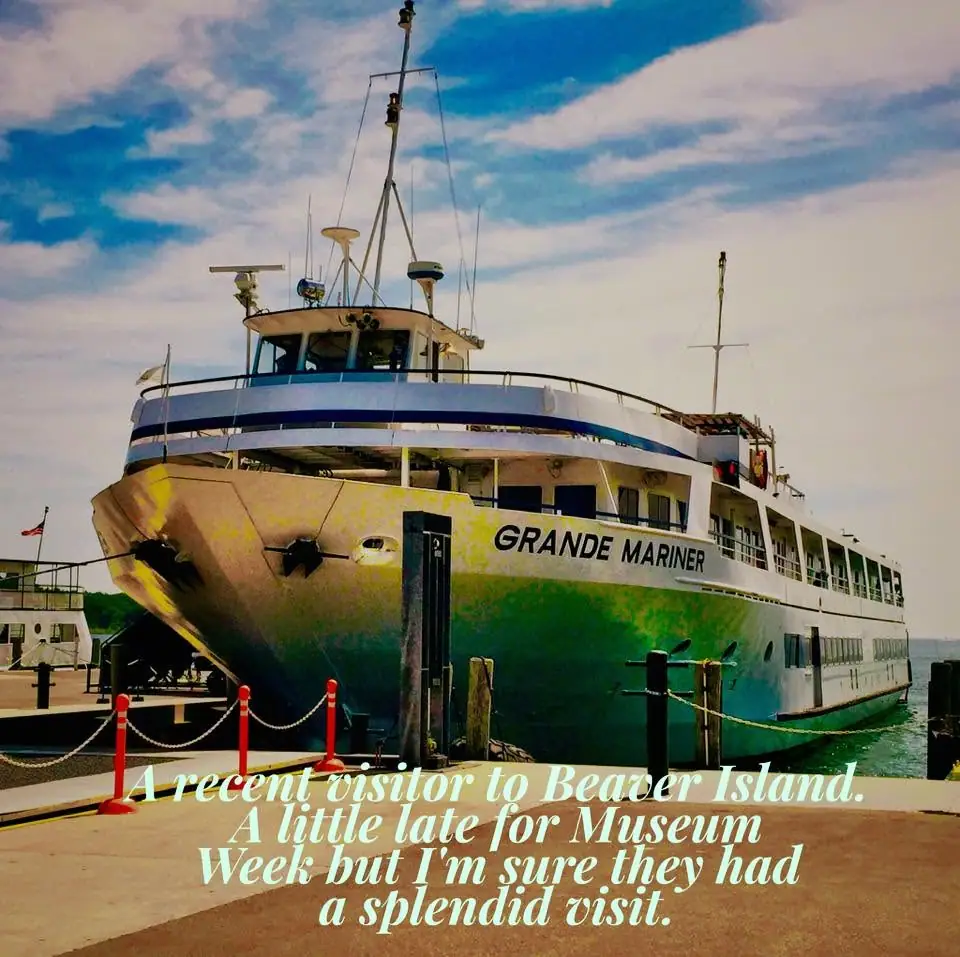 A large passenger ferry with green hull and blue stripe is moored beside a dock under a partly cloudy sky.