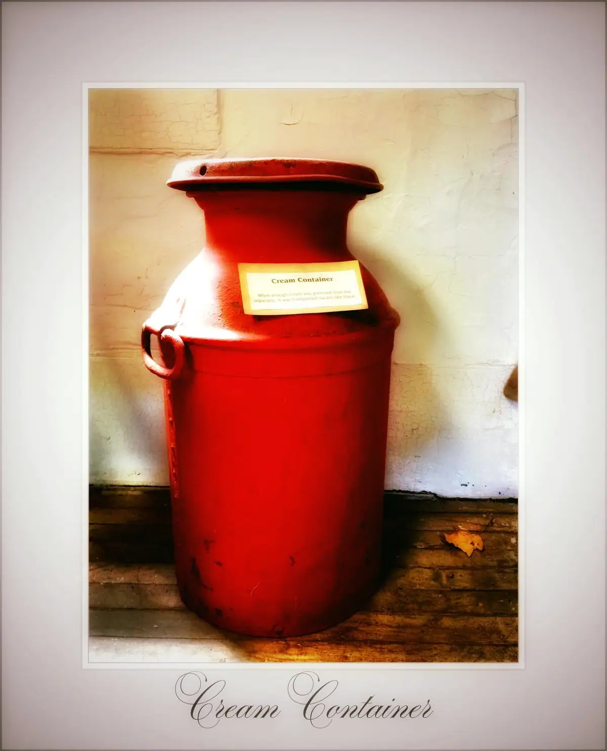 A large red metal cream container stands on a wooden floor, with labels reading “Cream Container.”