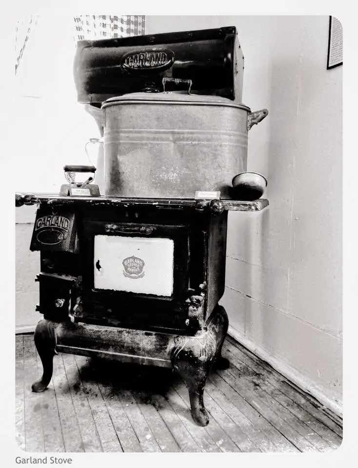 Black cast-iron stove with a large metal pot and smaller vessels displayed on a wooden floor.