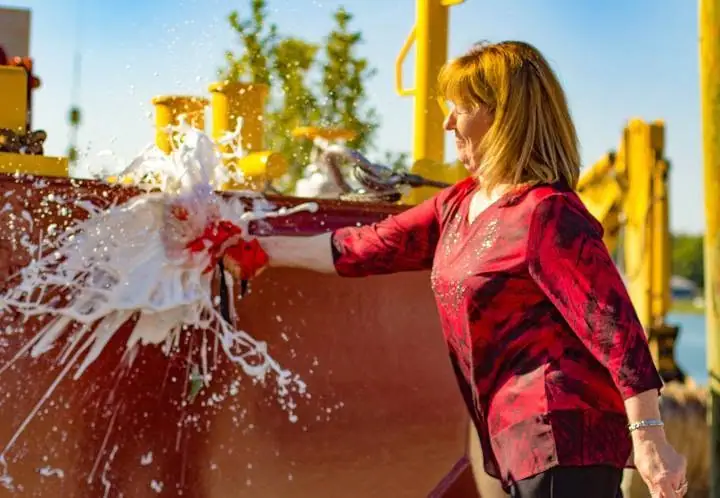 A woman in a red patterned shirt operates a water feature, sending a large spray into the air.