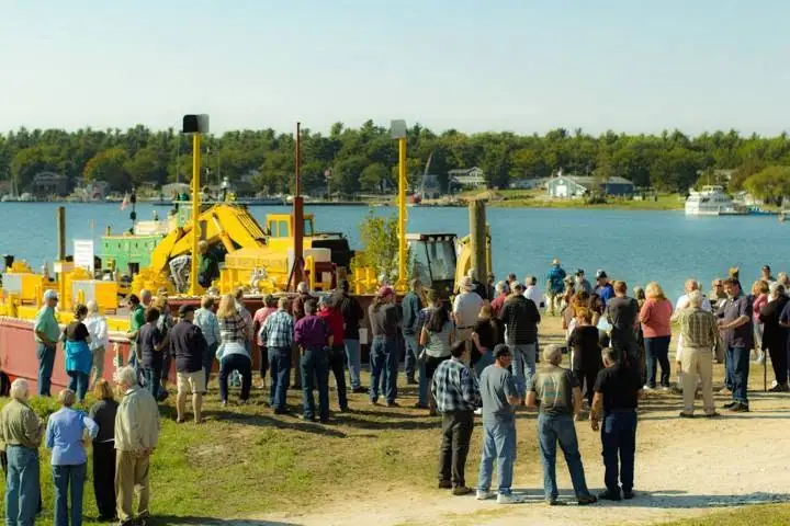 A crowd watches yellow heavy equipment positioned beside the water.