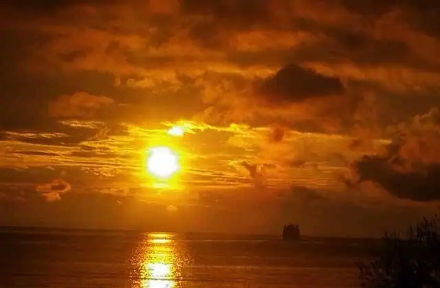 Sunset light reflects across the water as a large vessel appears on the horizon.