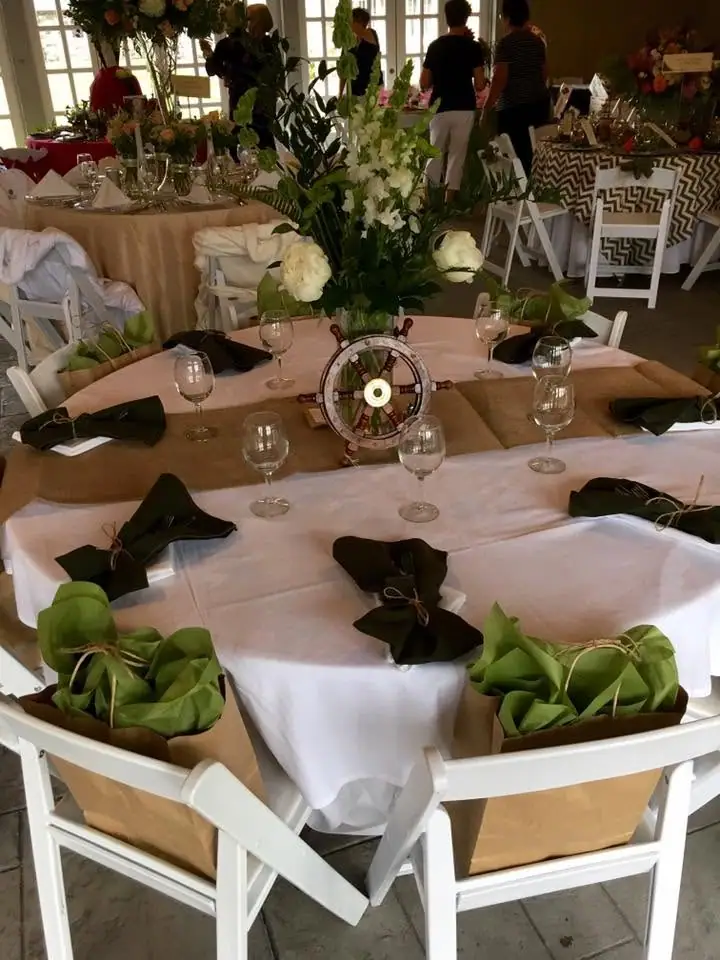 Banquet tables decorated with flowers, greenery, glassware, and a ship’s wheel centerpiece.