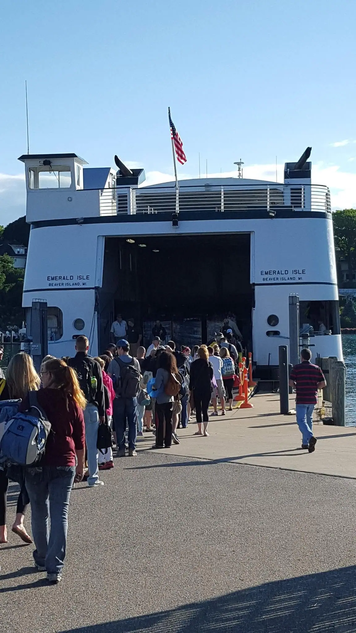 A crowd boards a white ferry through its open stern loading bay.