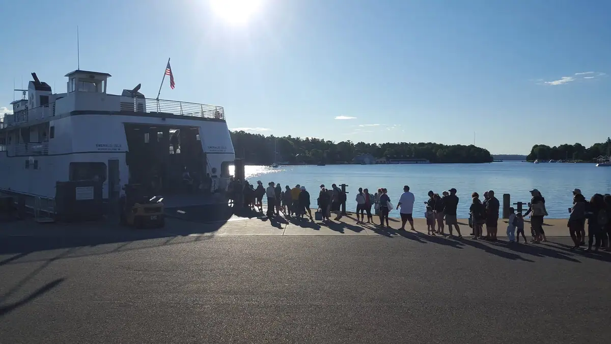 A passenger ferry is docked beside a pier while people gather along the waterfront.