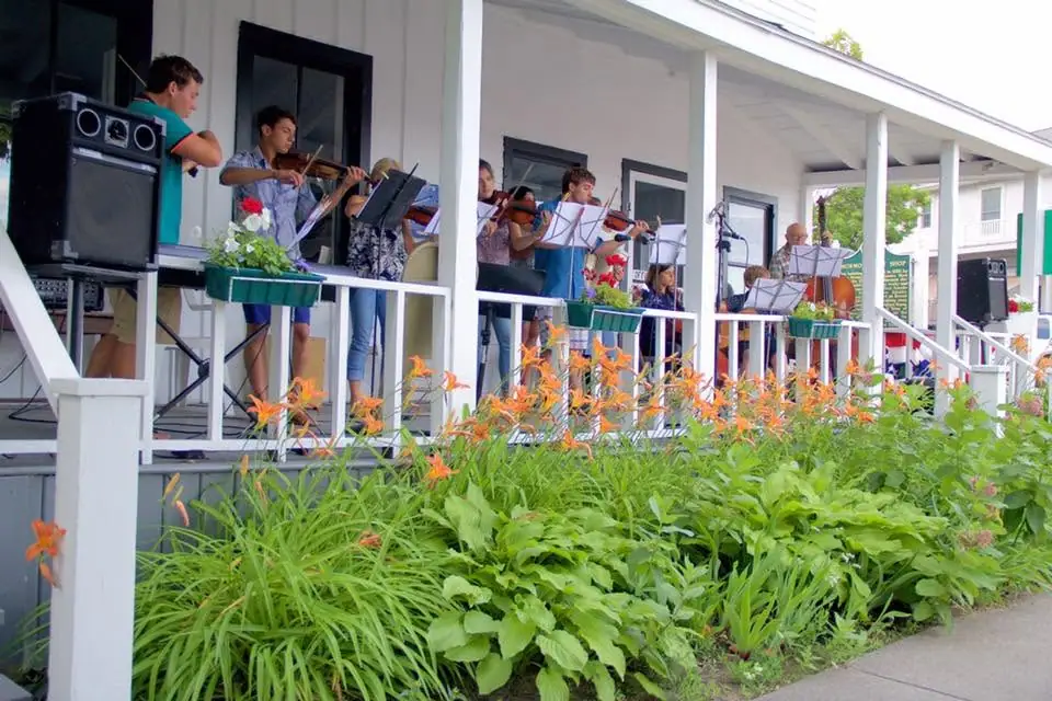 A string ensemble performs on a porch beside a garden of orange lilies.