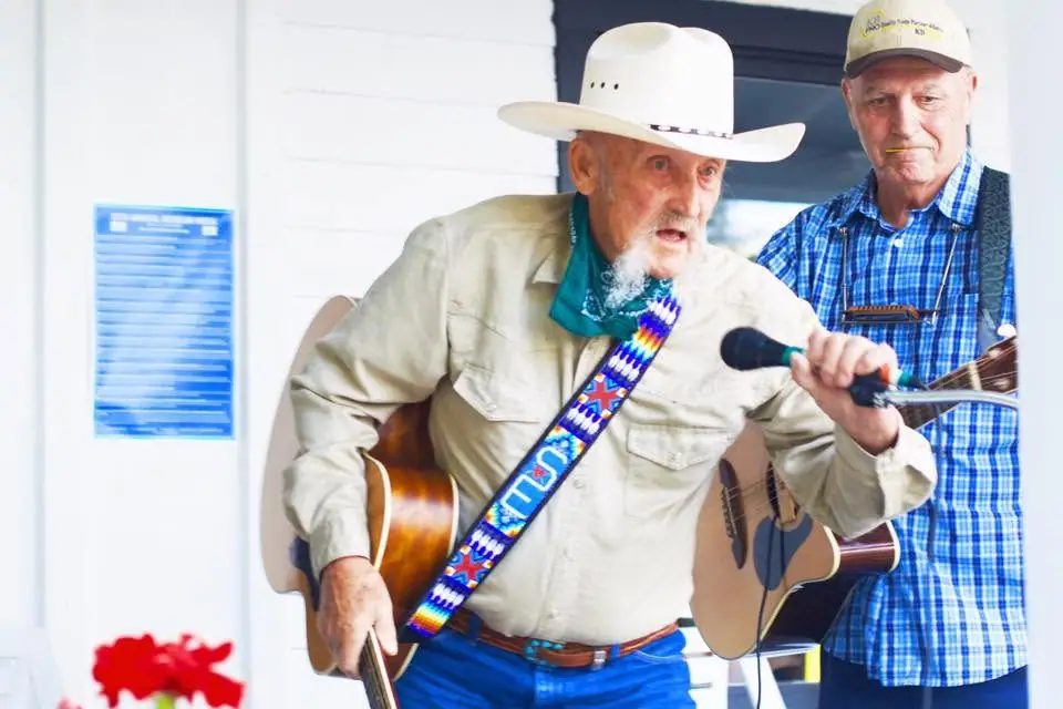 Two men perform outdoors with guitars and a microphone.